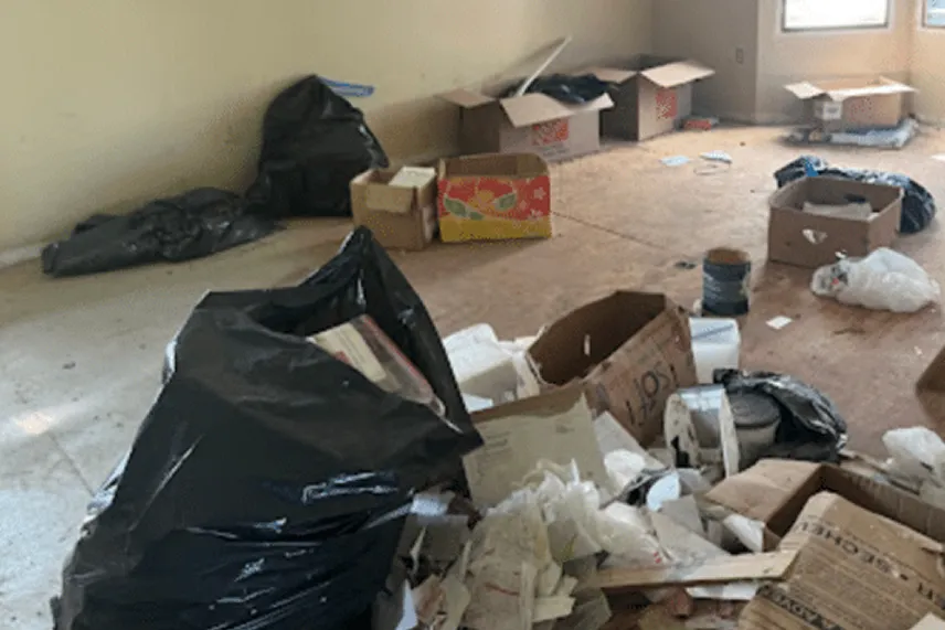 Cluttered interior space with trash bags, cardboard boxes, and debris, illustrating a home in need of cleanup and repairs, relevant to Portland Cash Buyers' services for selling houses as-is.