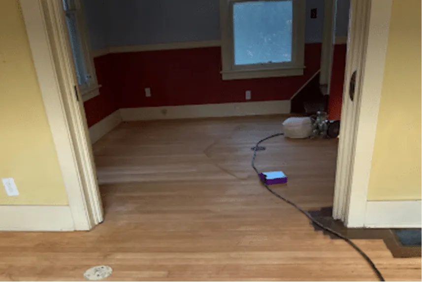 Interior view of a room with hardwood flooring, featuring yellow and red walls, a visible electrical outlet, and a power cord on the floor, illustrating the condition of homes sold as-is by Portland Cash Buyers.