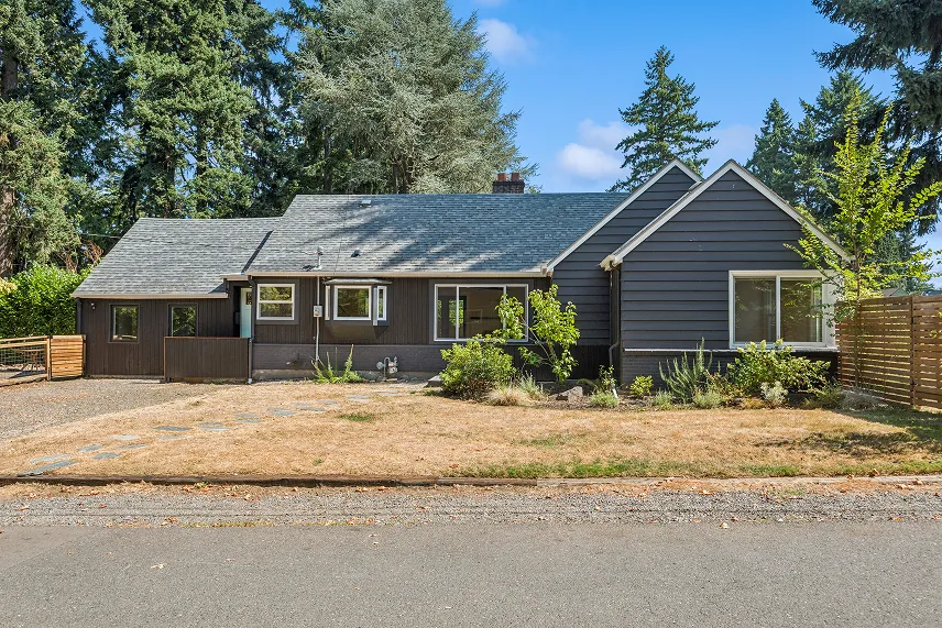 Single-story house with a gray exterior, surrounded by greenery and a gravel pathway, representing Portland Cash Buyers' commitment to buying homes as-is for cash offers.