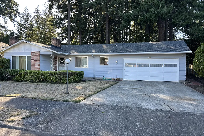 Single-story blue house with a white garage door and manicured front yard, surrounded by trees, representing a property available for quick cash sale by Portland Cash Buyers.