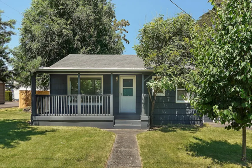 Front view of a dark blue house with a porch, surrounded by greenery, representing Portland Cash Buyers' commitment to purchasing homes as-is for cash offers.