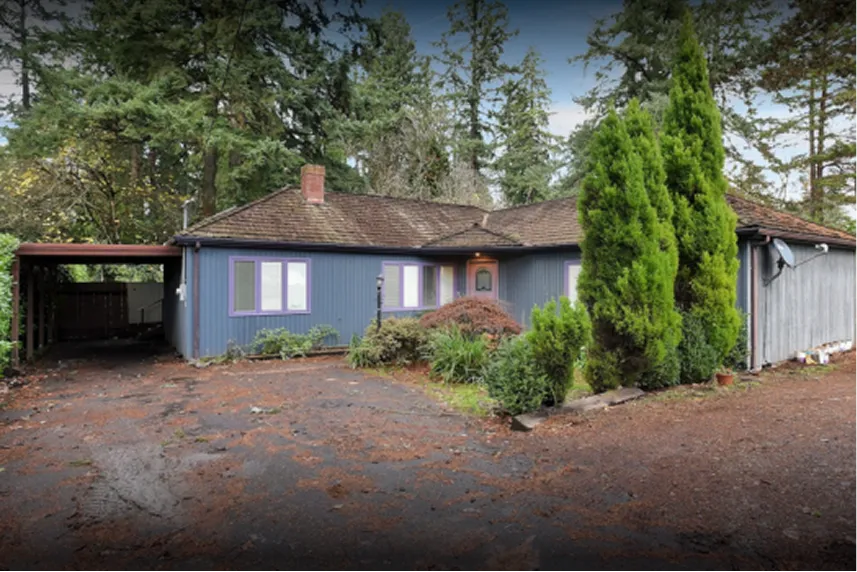 House exterior in Portland, surrounded by greenery, featuring a blue facade, purple-trimmed windows, and a carport, representing properties sold as-is by Portland Cash Buyers.