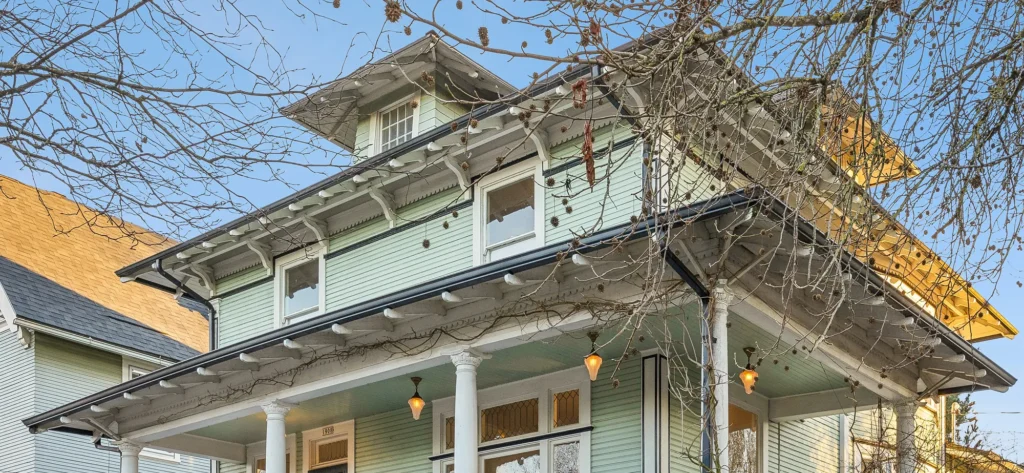 Historic Portland home with a light blue exterior, intricate architectural details, and decorative eaves, surrounded by leafless trees, representing properties bought by Portland Cash Buyers.